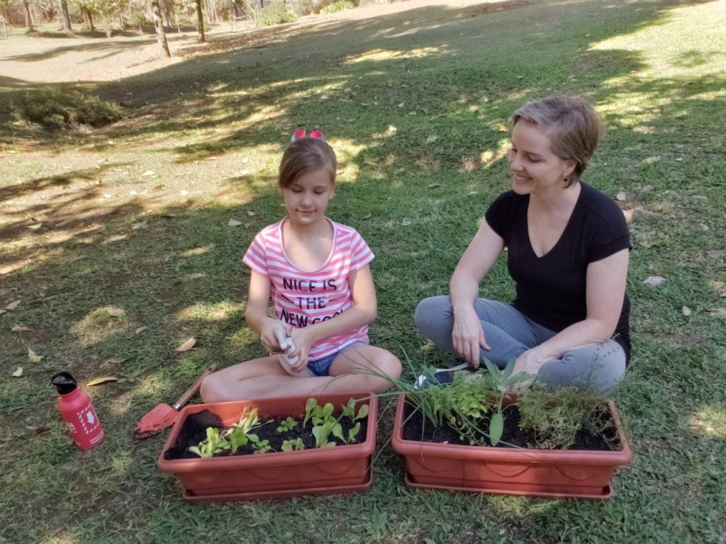 Mãe e filha sentadas na grama montando a horta em casa